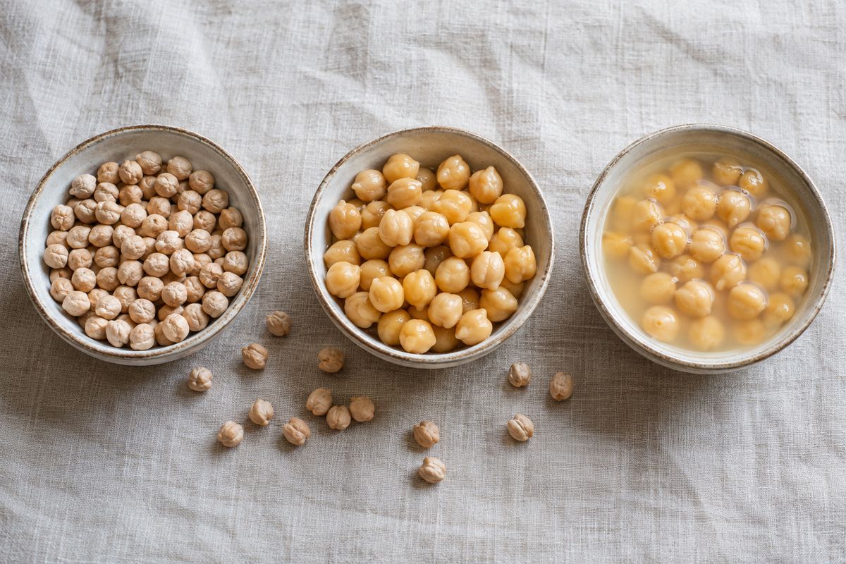 Three bowls in a row on linen: hard dry chickpeas, plump cooked chickpeas, and chickpeas sitting in cloudy canning liquid.